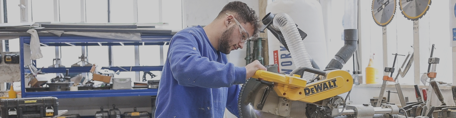 A handyman operates a saw, skilfully cutting through a piece of wood in a workshop setting for a home improvement job