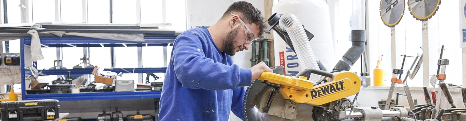 A man operates a saw, skilfully cutting through a piece of wood in a workshop setting