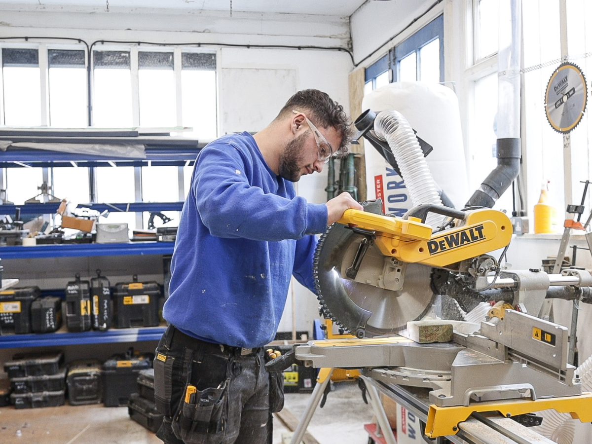 A man operates a saw, skilfully cutting through a piece of wood in a workshop setting