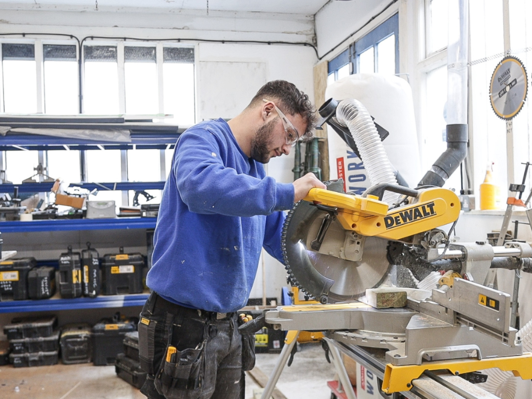 A handyman operates a saw, skilfully cutting through a piece of wood in a workshop setting for a home improvement job