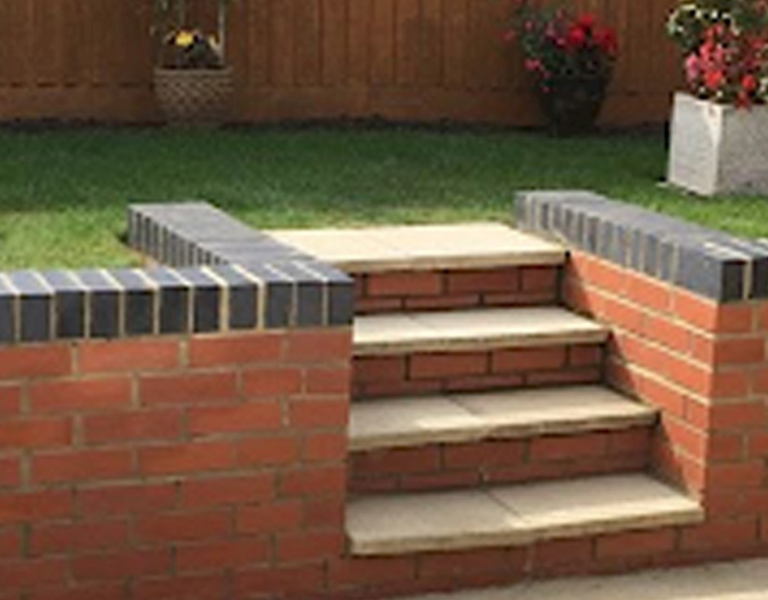 Garden with a raised lawn, surrounded by a brick retaining wall with tiled edges and steps leading to the grass area, ideal for landscaping and outdoor improvements