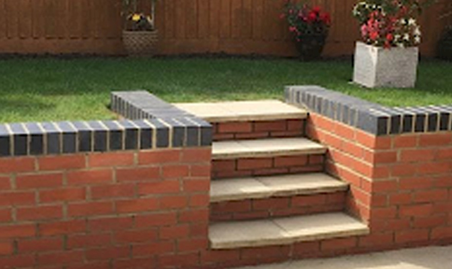 Garden with a raised lawn, surrounded by a brick retaining wall with tiled edges and steps leading to the grass area, ideal for landscaping and outdoor improvements