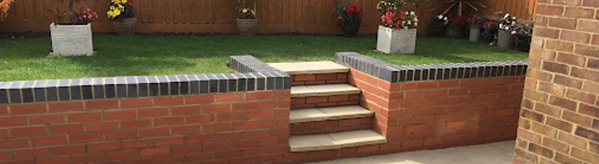 Garden with a raised lawn, surrounded by a brick retaining wall with tiled edges and steps leading to the grass area, ideal for landscaping and outdoor improvements