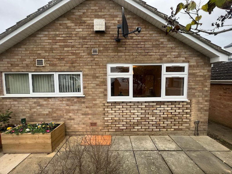 brick house with white-framed windows, a small raised flower bed, and a paved patio area, perfect for patio and garden maintenance services