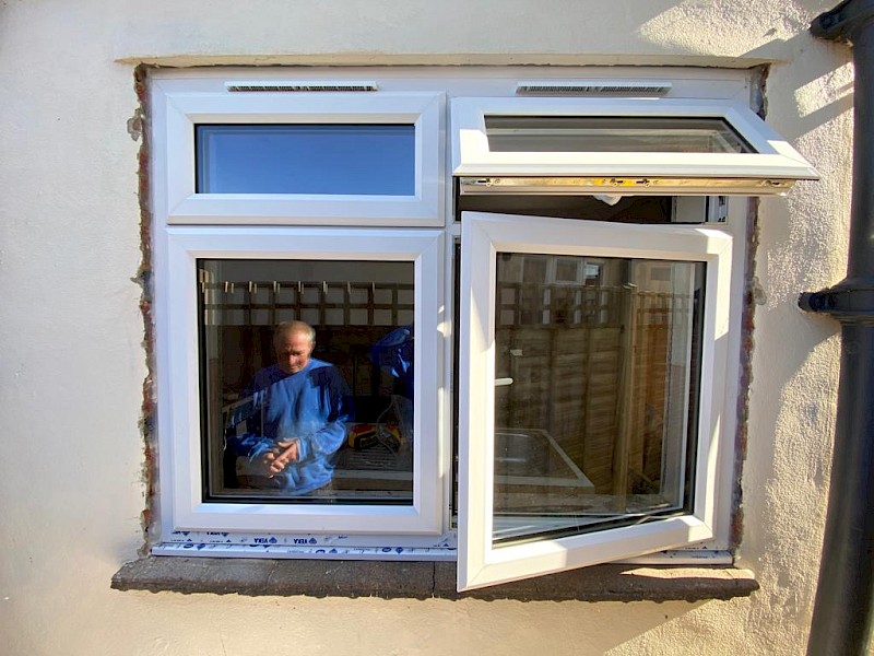 Handyperson in reflection of recently fitted new white double glazed windows