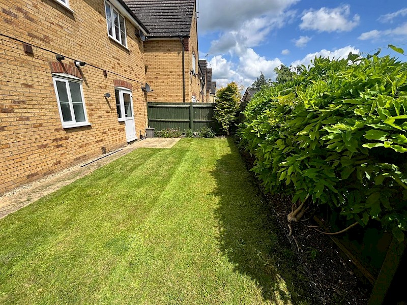 Well-maintained backyard with a freshly mowed lawn, bordered by a hedge and brick house, ideal for showcasing lawn care and gardening services.