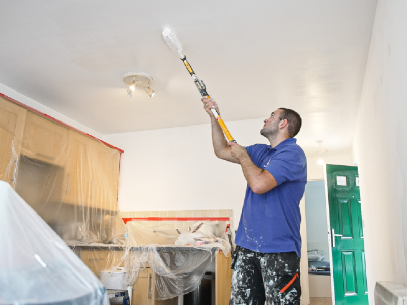 Handyperson using a long paint roller to paint and decorate inside a home