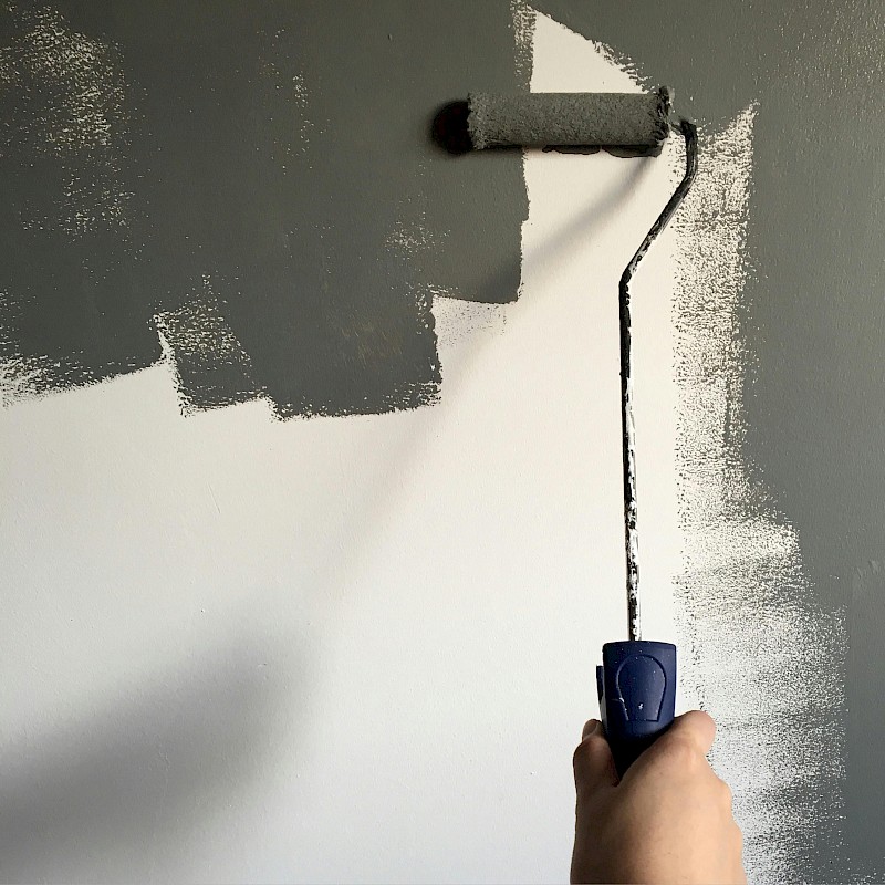 Paint roller painting a white wall dark grey